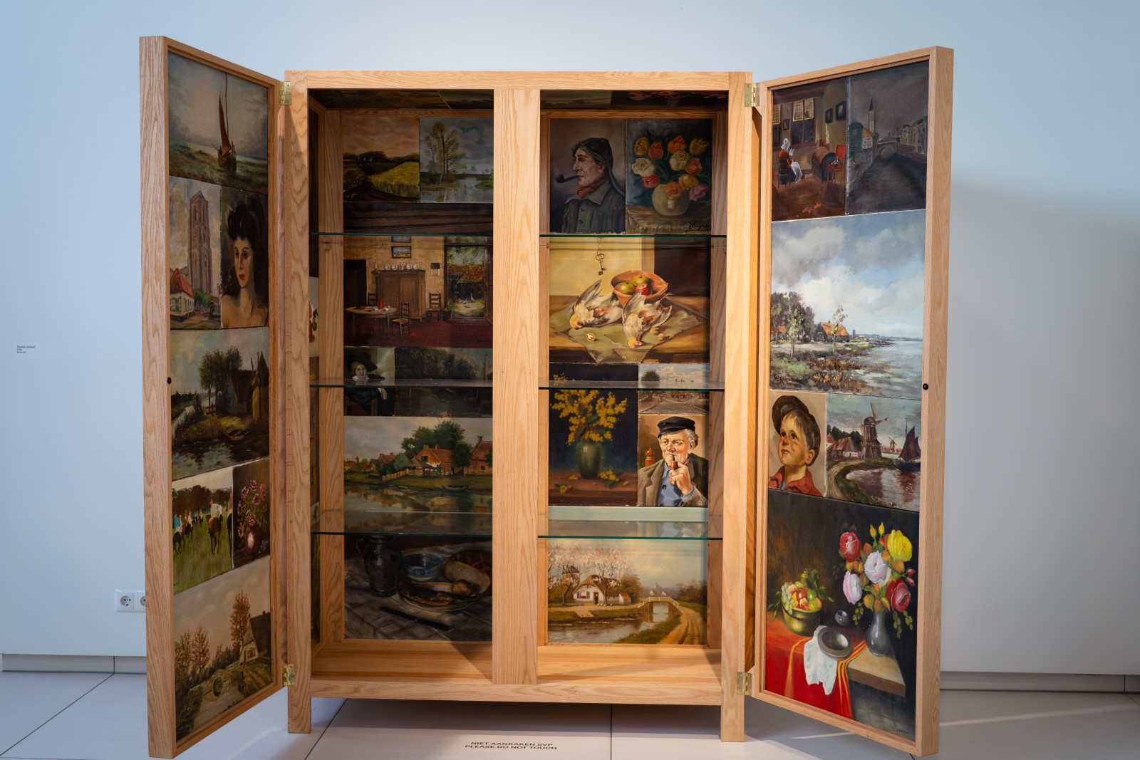 Wooden cabinet lined with small paintings in an exhibition at Museum JAN