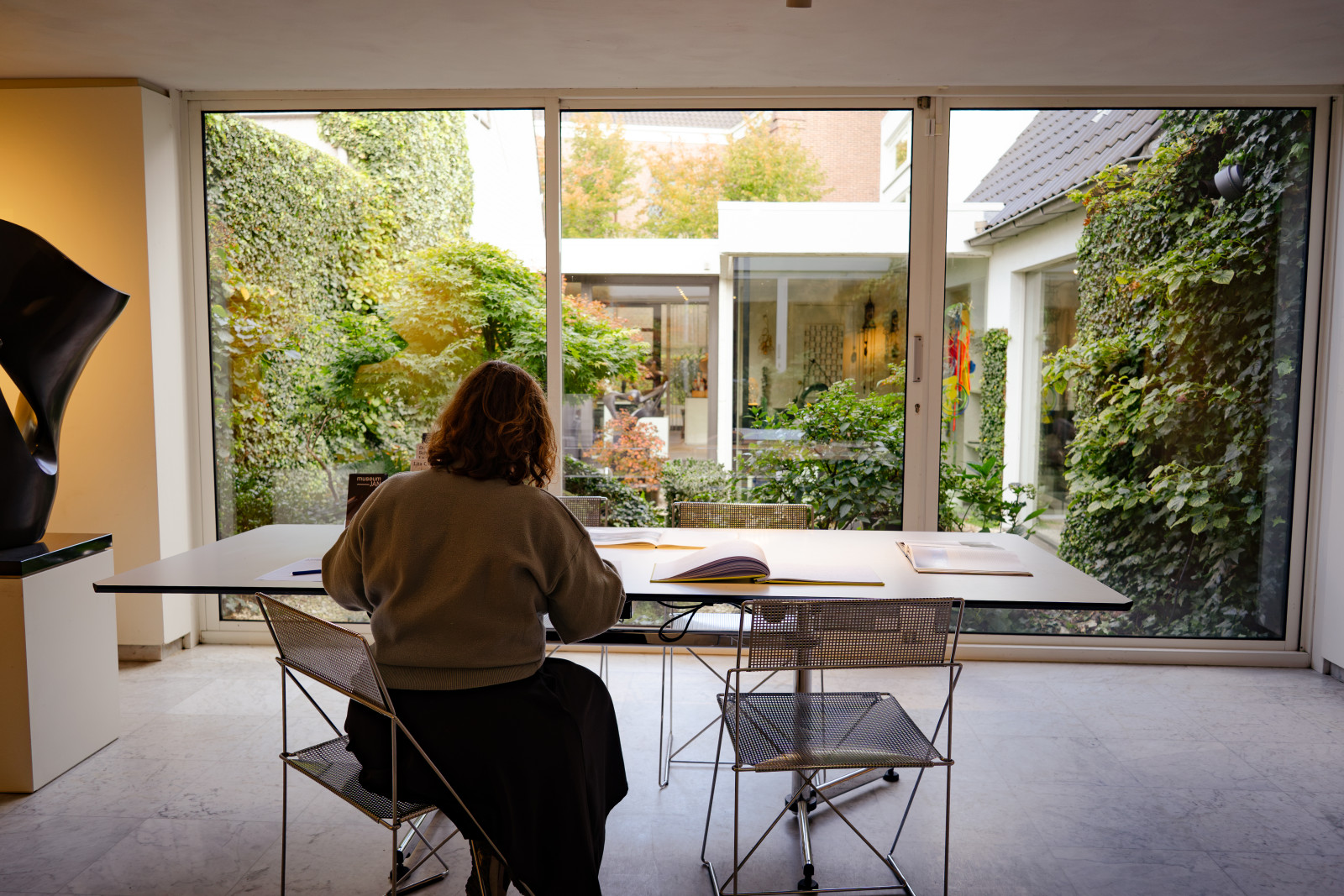 Visitor reading at a table by a window onto Museum JAN's green courtyard