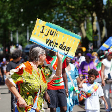 Marcher holding a '1 juli vrije dag' sign at the Bigi Spikri parade, Amsterdam