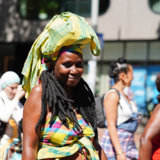 Smiling woman in a yellow koto headwrap at the Bigi Spikri parade, Amsterdam