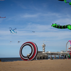 Striped ring kite on the sand and kites flying by De Pier