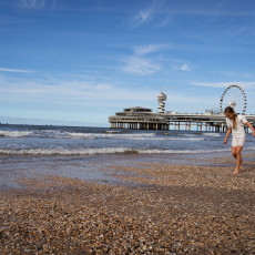 Girl walking on the shells at the water's edge, with De Pier behind