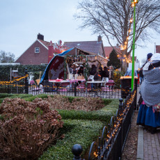 Villagers in period dress passing a clipped box garden and a lit stall in De Rijp