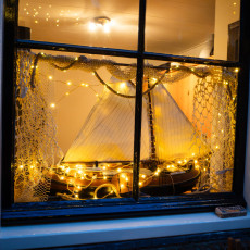 A model sailing ship framed by fishing net and fairy lights in a De Rijp window
