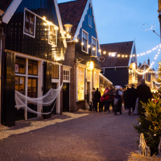 A fishing net hung on a black timber house as visitors walk a De Rijp street