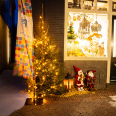 A lit tree and two Father Christmas figures on straw outside a De Rijp shop