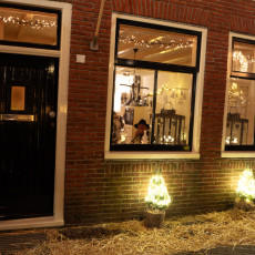 Lanterns in the window and small lit trees on straw outside a De Rijp house
