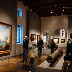 Visitors looking at a sea battle painting and an old cannon in the museum galleries