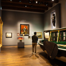 Museum room with a gilded ceremonial sloop, a portrait and a carved figurehead