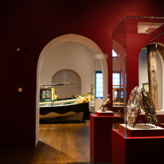 Red-walled gallery with silver display cases and a gilded sloop through the arch