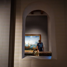 Visitors framed by a wall opening as they look at a seascape and a bronze cannon