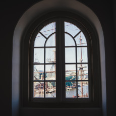 Arched museum window looking out on the masts of ships moored at the quay