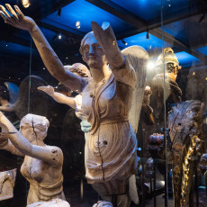 Winged figurehead with a raised arm among other carvings in a display case