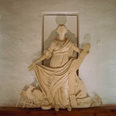 Plaster relief of a classical figure with an anchor, set against a white wall