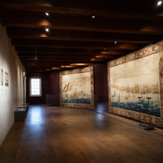 Large woven tapestries of naval scenes hanging in a beamed museum hall