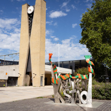 A concrete clock tower and a sculpture wrapped in a carnival scarf