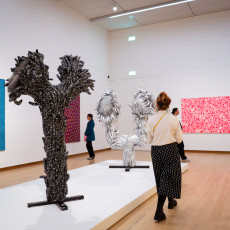 Silver accumulation sculptures standing between Kusama's blue and pink paintings