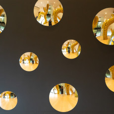 Round mirrors in a dark wall reflecting Kusama's yellow dotted installation