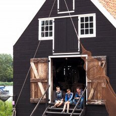 Visitors sitting on the steps of a black timber net shed in the Zuiderzee Village