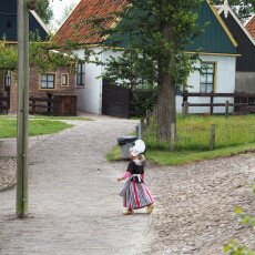 Girl in traditional Dutch costume walking a cobbled lane in the Zuiderzee Village