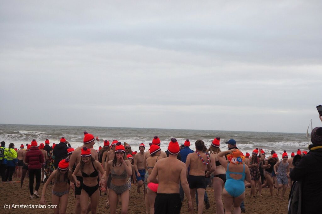 A crowd of people in swimsuits and red hats gather on a beach for the New Year's Dive at Scheveningen, Netherlands