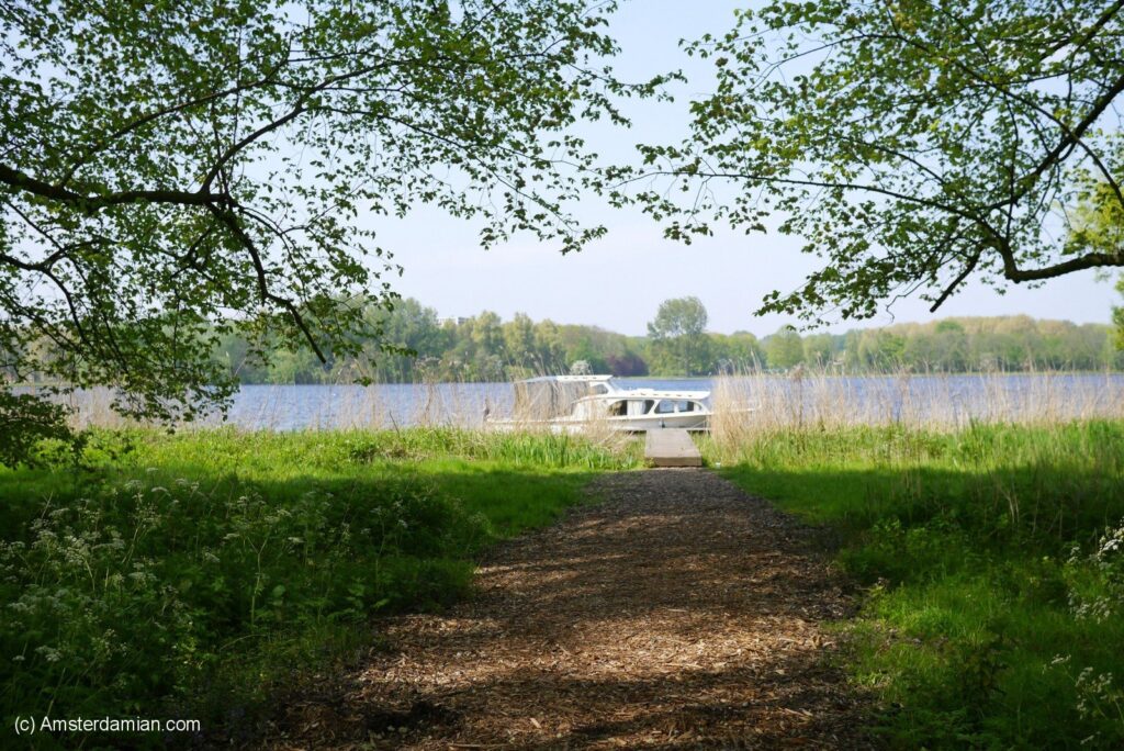 A serene path leads through lush greenery towards a tranquil lake at Sloterplas in Amsterdam, Netherlands
