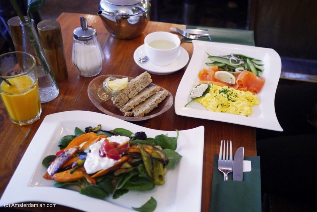 A vibrant breakfast spread featuring a green salad, smoked salmon, scrambled eggs, and toast on white plates with a wooden table backdrop