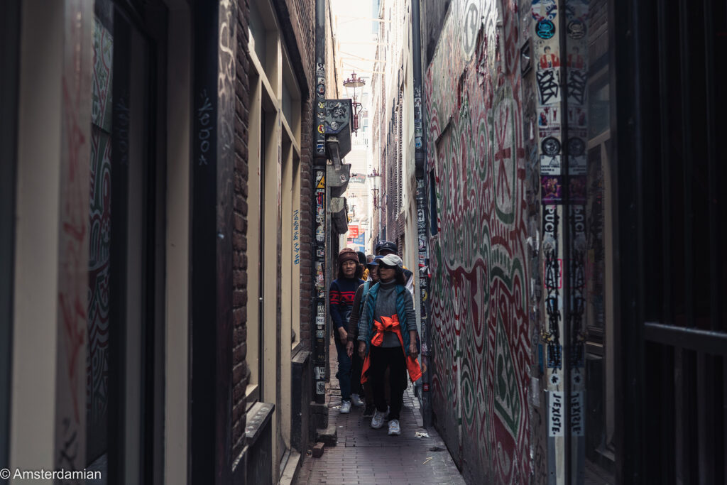 Tourists walking on Trompettersteeg, the narrowest street in Amsterdam