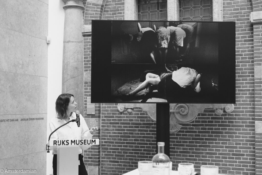A speaker at a Rijksmuseum lectern addresses guests at the press preview, with Ed van der Elsken's photographs shown on a large screen behind her.