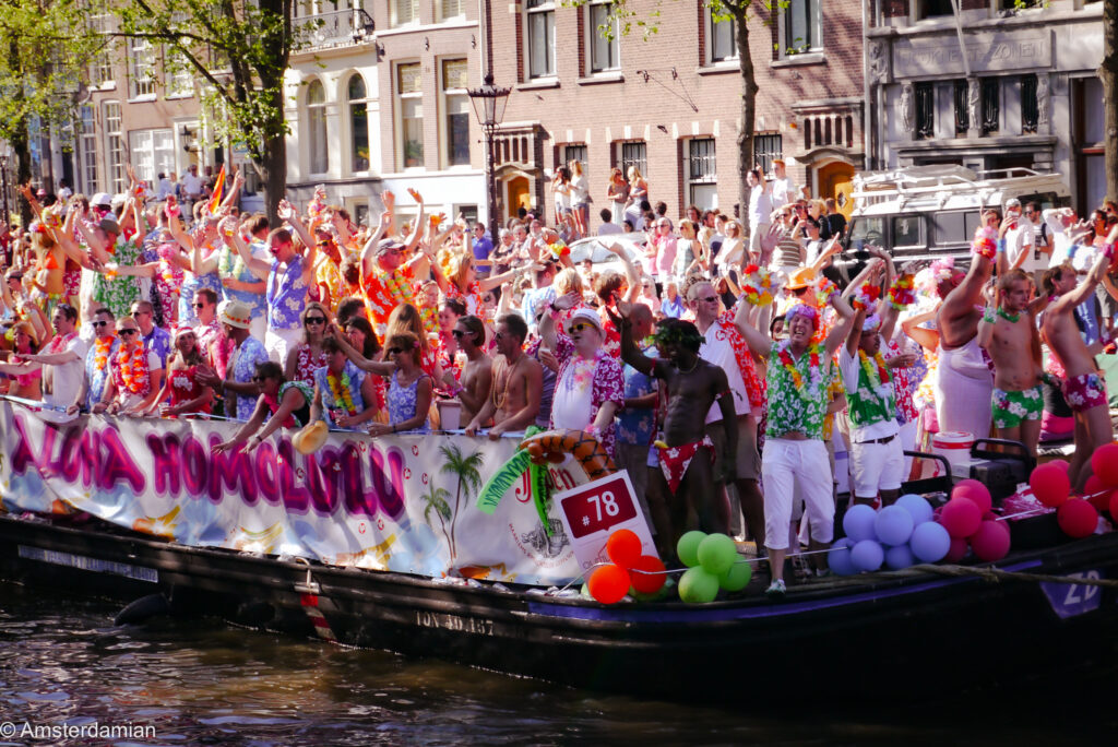 Parade boat with Aloha Homolulu banner and passengers in Hawaiian shirts and flower garlands