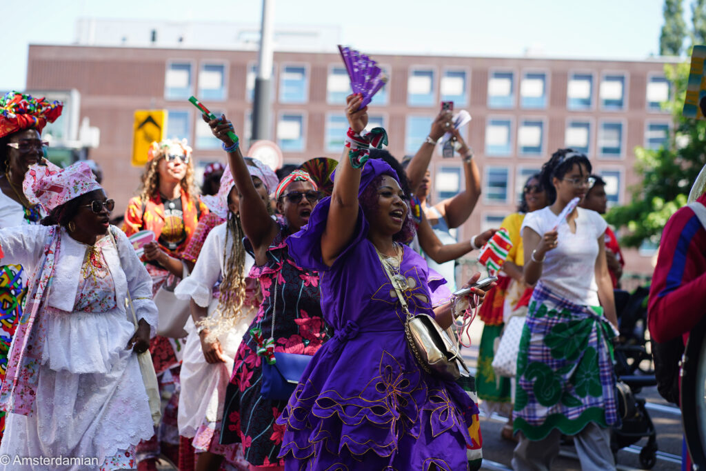 Women in colourful koto dresses waving fans at the Bigi Spikri parade in Amsterdam