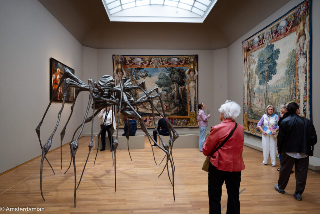 Skylit exhibition room with Louise Bourgeois's giant spider, tapestries and visitors