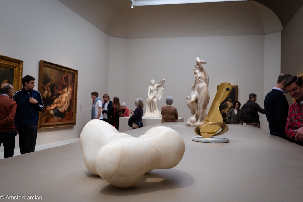 White biomorphic marble sculpture in the foreground, with a gleaming bronze and plaster statues behind