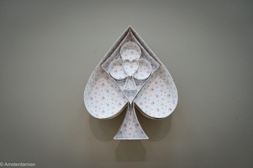 Spade-shaped wall sculpture in floral fabric holding a club and a heart
