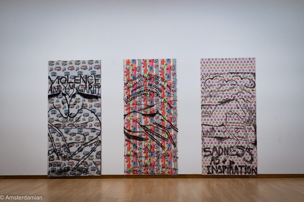 Three patterned fabric panels with drawings and slogans like sadness as inspiration
