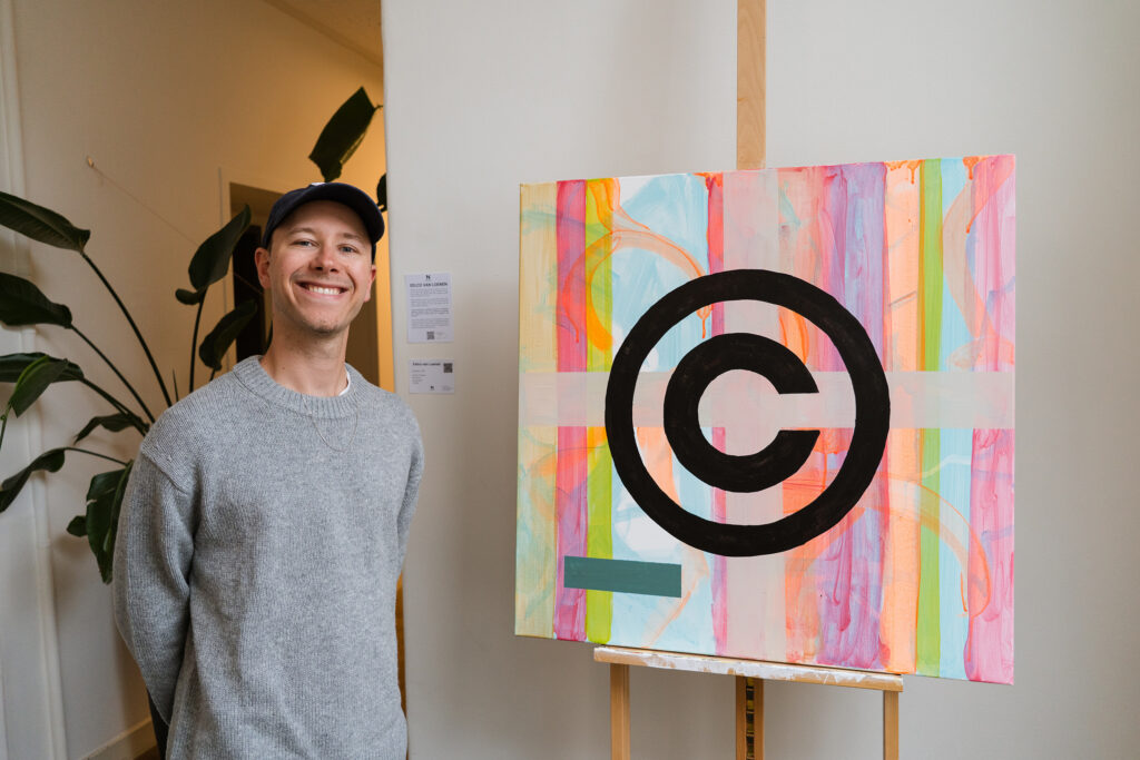 Jasha Berkenbosch beside a colourful painting with a copyright symbol
