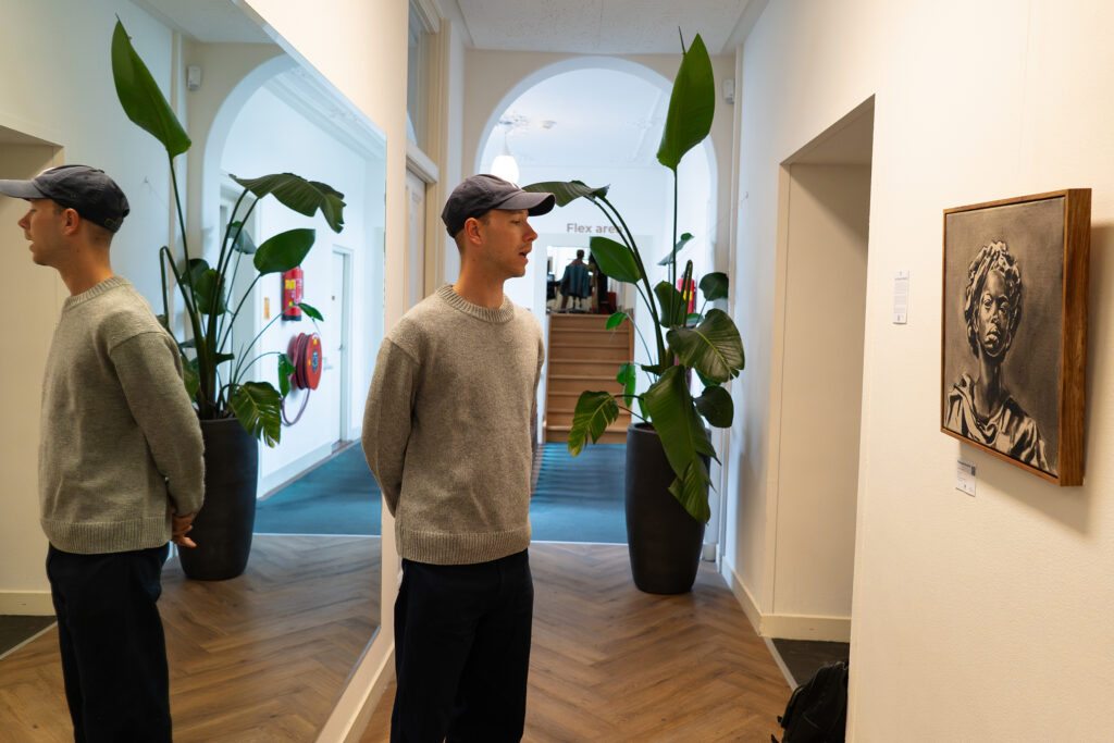 Jasha Berkenbosch looking at a painted portrait in an office corridor
