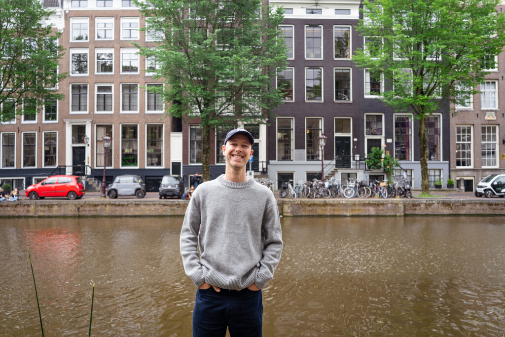 Jasha Berkenbosch smiling by an Amsterdam canal, canal houses behind him