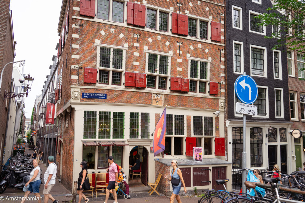 Historic red-shuttered corner house on Oudezijds Voorburgwal as festivalgoers walk past