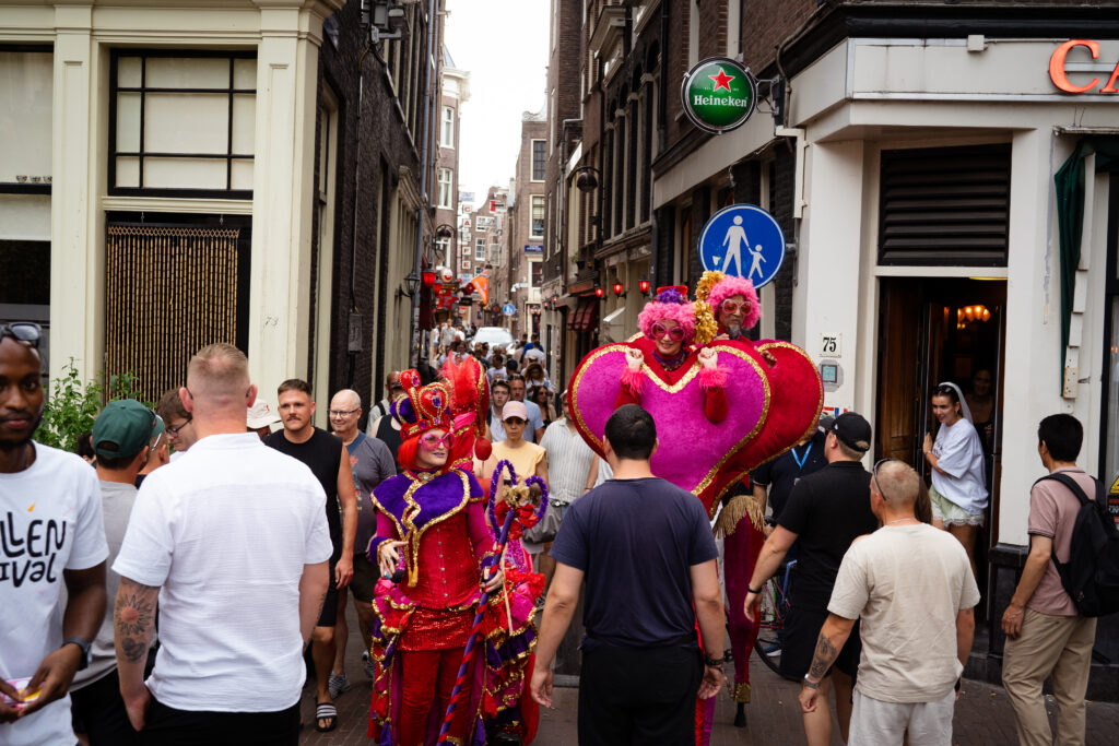 Costumed heart and jester performers moving through a crowded Red Light District alley