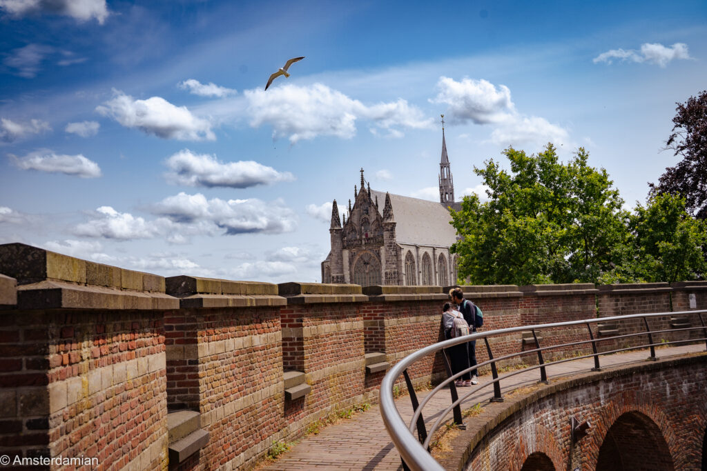 A church rising beyond a brick city wall walkway in Leiden under a blue sky