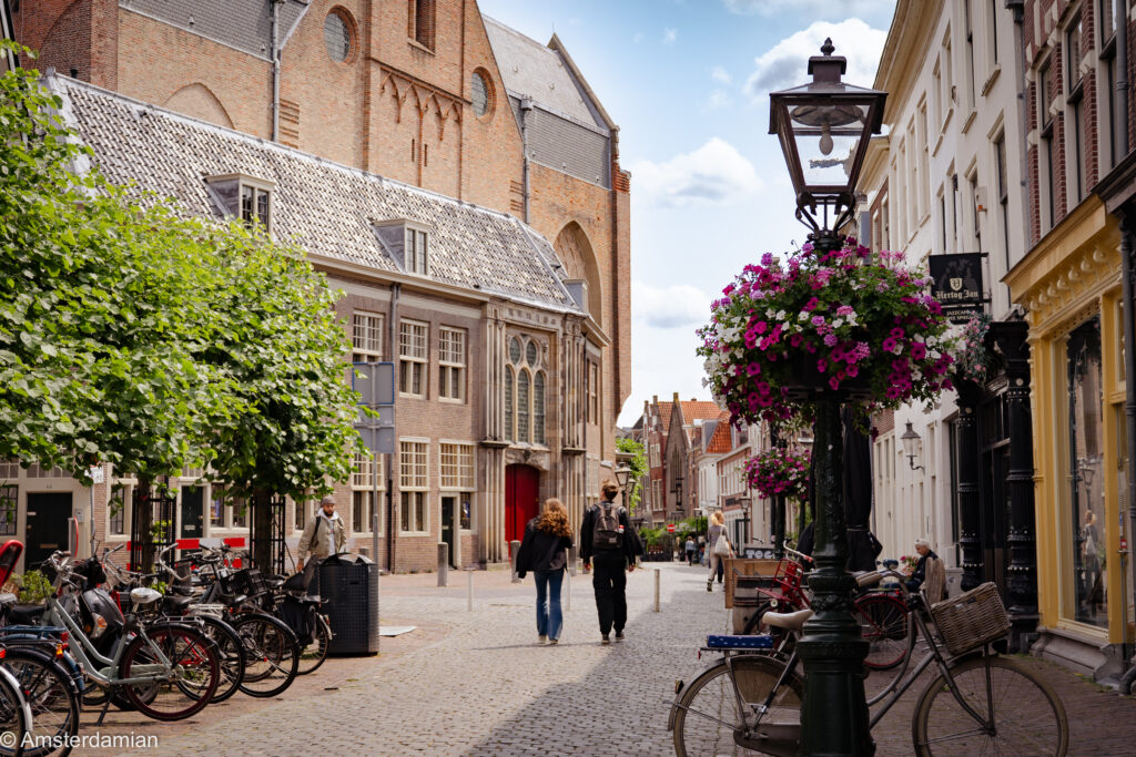 Cobbled old-town street with a brick church, parked bikes and a flower-decked lamppost on a day trip