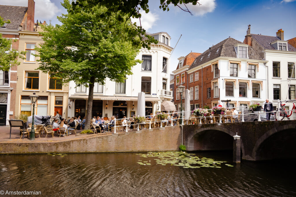 Cafe terrace beside a canal and stone bridge among elegant white houses on a sunny summer day