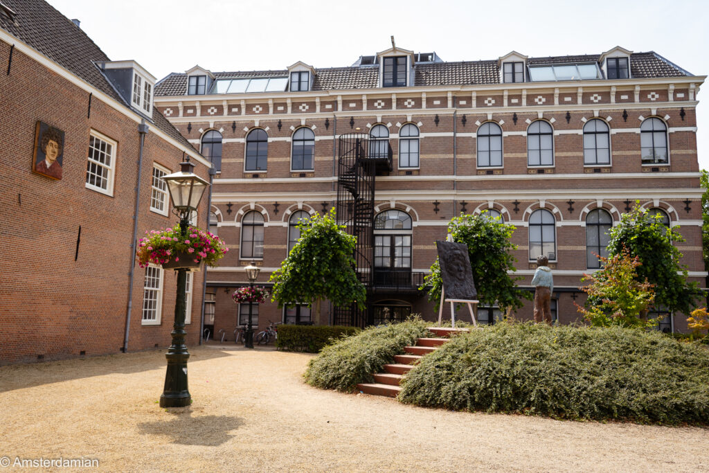 Sunlit courtyard by a grand brick building with a portrait plaque and an artist's easel in Leiden