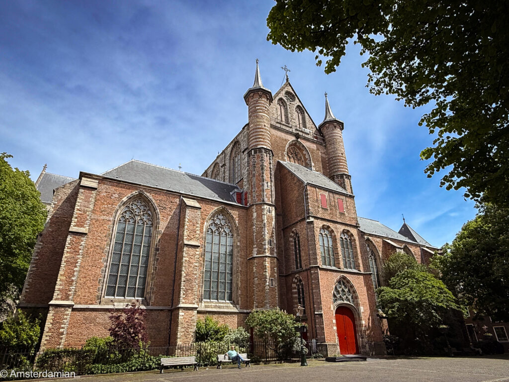 The brick Gothic Pieterskerk with stair turrets and a red door under a blue sky in Leiden