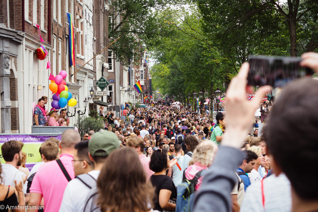 Crowded street party with rainbow flags and balloons on the facades during Pride week