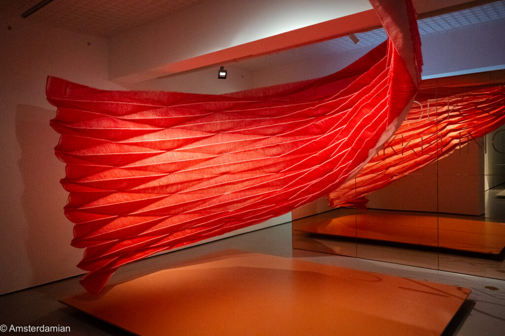 Large pleated red textile installation suspended in a gallery at the TextielMuseum, Tilburg