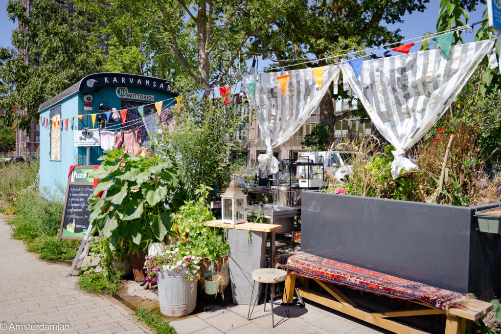Vittorio Outdoor cafe kiosk with bunting, potted plants and a rug-covered bench in Tilburg