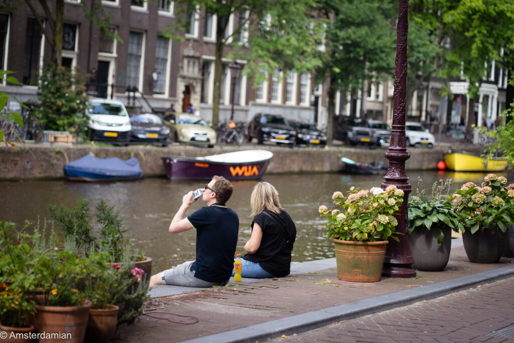 Two people sitting on canal's edge in Amsterdam