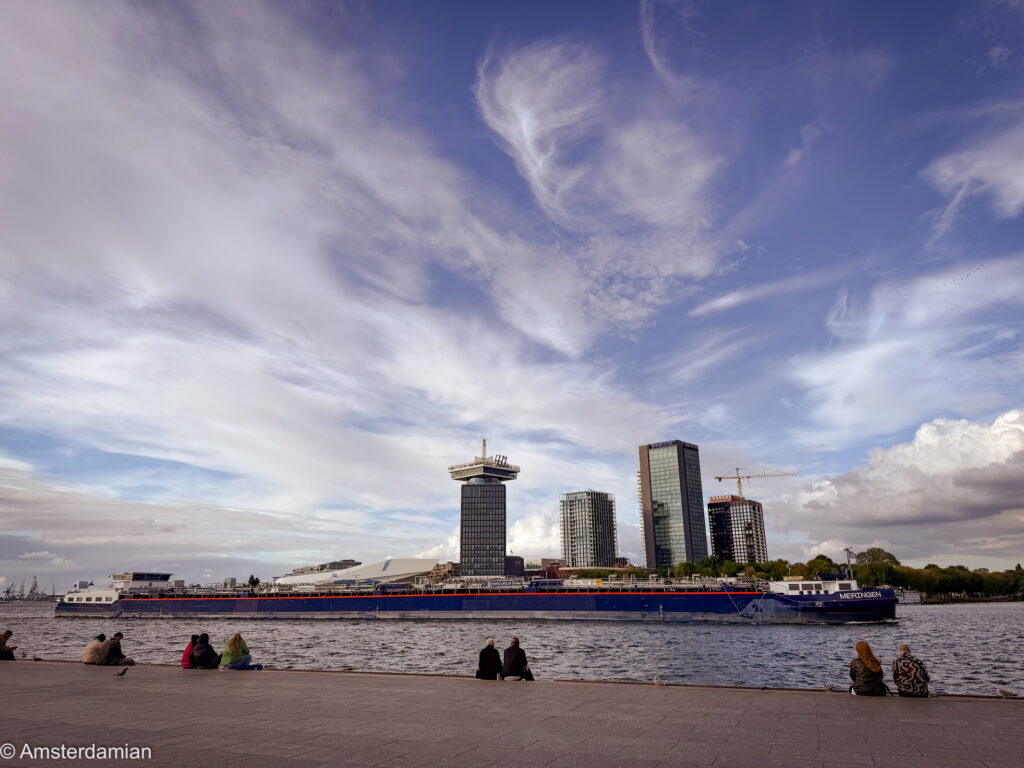 People sitting on the waterfront behind Central Station looking at Amsterdam Noord